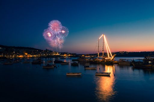 A night view of Valencia port with boats and water reflecting lights, firework in the clear sky