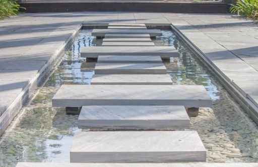 A beautiful view of an empty fountain with marble panels and a stone tiled in the park on a sunny day
