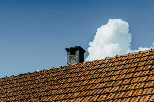 A low angle shot o the roof and the chimney under the sky with puffy clouds