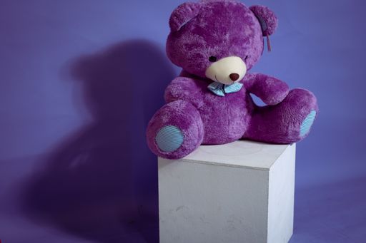 An adorable purple teddy bear toy on a white cube