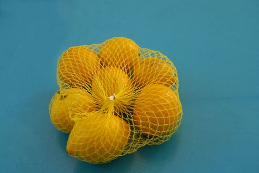 A closeup shot of oranges in a yellow net bag isolated on blue background