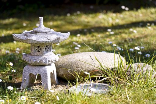 A closeup shot of a marble Japanese lantern in grass and daisies