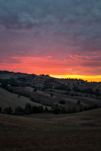 A beautiful view of the green hills gleaming under the shiny cloudy sky during sunset in Tuscany