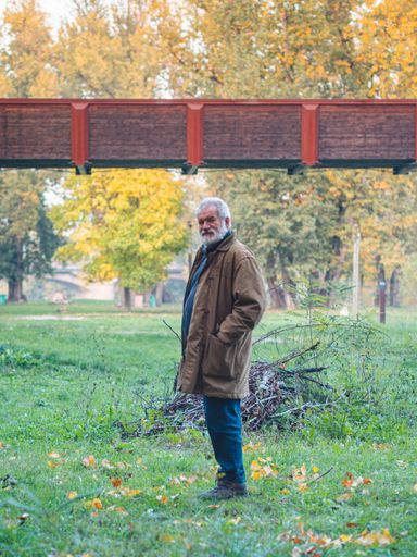 A vertical shot of an elderly caucasian man standing on the grass with fallen leaves in the park