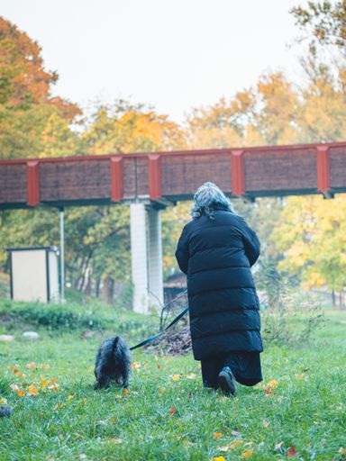 A vertical shot of a female in a black coat walking in the park with her dog