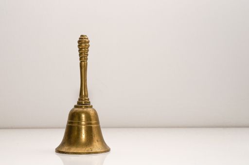 A closeup shot of a golden handbell on a white wall background