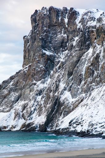 A vertical shot of rocky and snowy cliffs at the Kvalvika beach in Lofoten, Norway