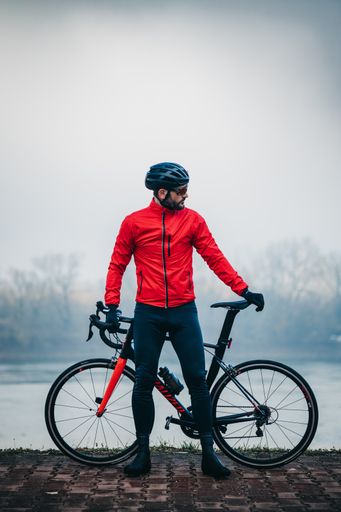 A young cool male cyclist in red sportswear posing with his bicycle by the lake on a gloomy day