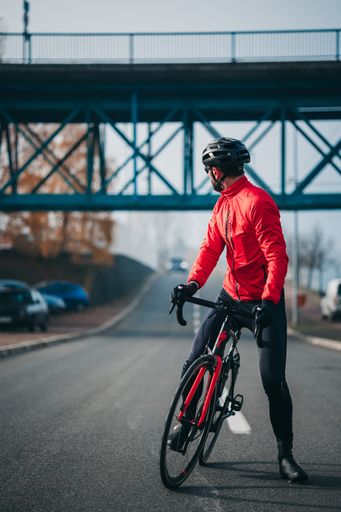 A front view of a young cool male cyclist in red sportswear riding a bicycle on a gloomy day