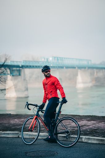 A side view of a young cool male cyclist in red sportswear riding a bicycle on a gloomy day