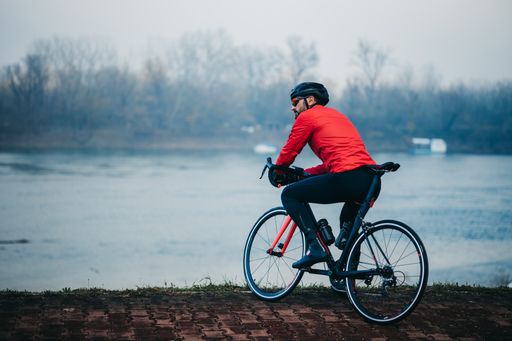 A side view of a young cool male cyclist in red sportswear riding a bicycle on a gloomy day