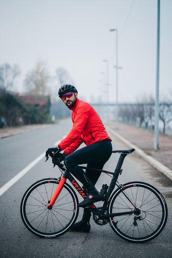 A side view of a young cool male cyclist in red sportswear riding a bicycle on a gloomy day