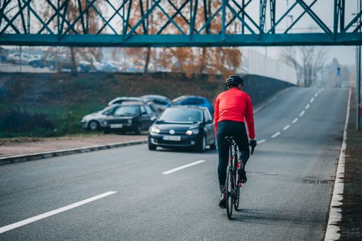 A back view of a young cool male cyclist in red sportswear riding a bicycle on a gloomy day