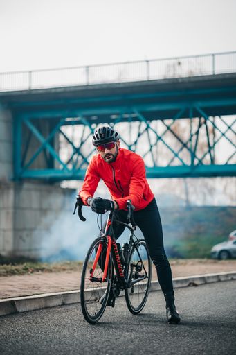 A front view of a young cool male cyclist in red sportswear riding a bicycle on a gloomy day