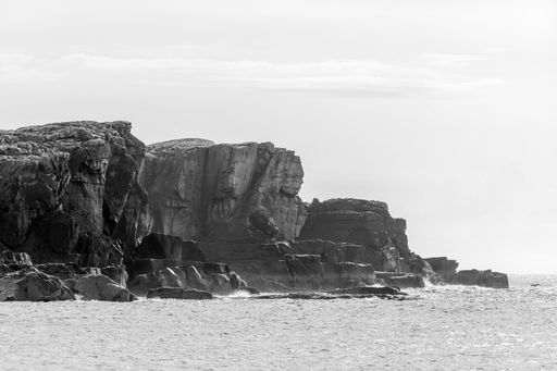 A grayscale shot of rocky coast under a white sky in Scotland