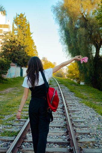 A vertical shot of a young stylish female posing outdoors with a red backpack on train tracks
