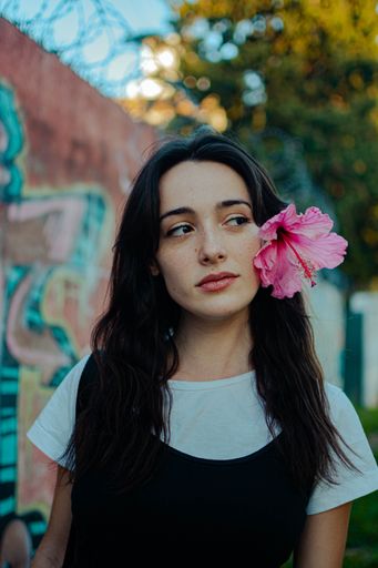 A vertical shot of a young beautiful female posing with a pink Hibiscus flower