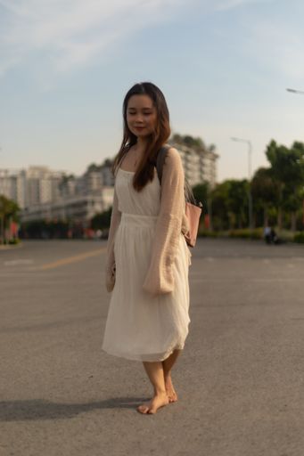 A vertical shot of an Asian female in a white dress posing in the street barefoot