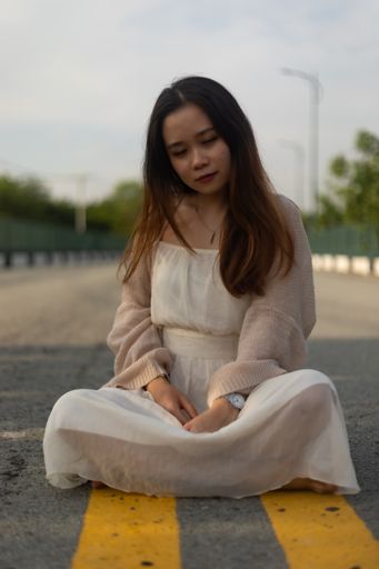 A vertical shot of a young Asian female sitting in the street cross-legged