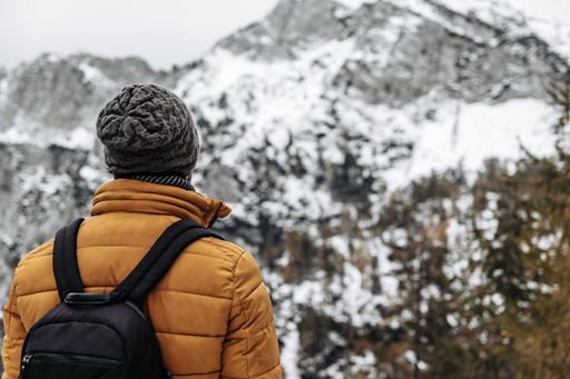 A back view of a Caucasian man with a backpack and winter clothes hiking in the Julian Alps in Slovenia