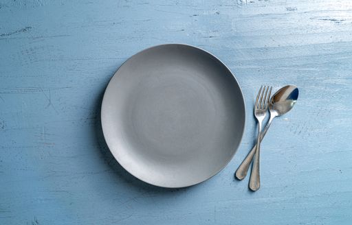 A top view of a plate with a fork and a spoon on a blue wooden table