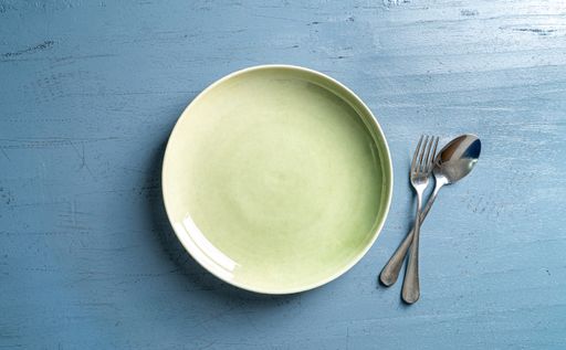 A top view of a plate with a fork and a spoon on a blue wooden table