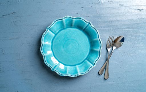 A top view of a plate with a fork and a spoon on a blue wooden table