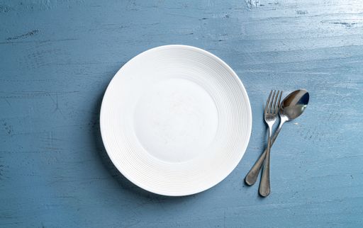 A top view of a plate with a fork and a spoon on a blue wooden table