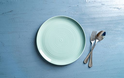 A top view of a plate with a fork and a spoon on a blue wooden table