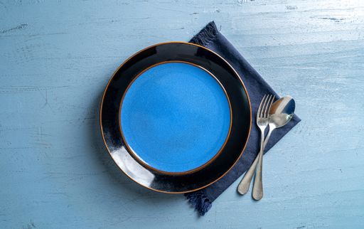 A top view of a plate with a fork and a spoon on a blue wooden table