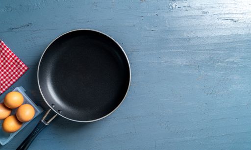 A top view of a black frying pan and eggs on a blue wooden table