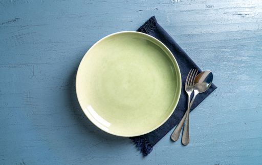 A top view of a plate with a fork and a spoon on a blue wooden table