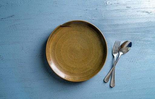 A top view of a plate with a fork and a spoon on a blue wooden table