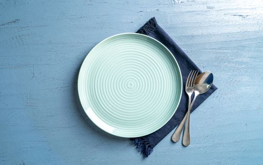 A top view of a plate with a fork and a spoon on a blue wooden table