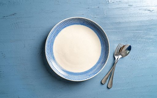 A top view of a plate with a fork and a spoon on a blue wooden table