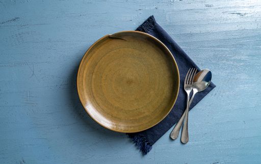 A top view of a plate with a fork and a spoon on a blue wooden table