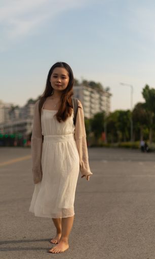 A vertical shallow focus shot of an Asian female wearing a white dress on the streets
