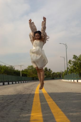 A vertical shallow focus shot of an Asian female jumping while wearing a white dress on the streets