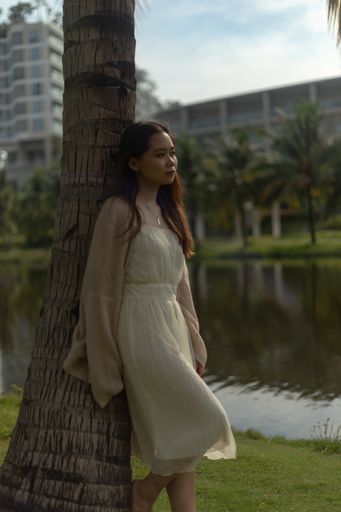 A vertical shallow focus shot of an Asian female wearing a white dress and laying on a tree