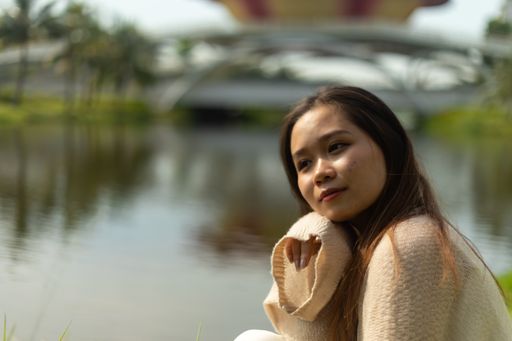 A shallow focus shot of an Asian female wearing a white dress by a lake