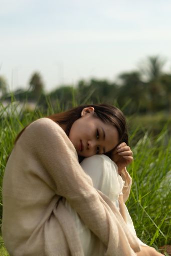 A shallow focus on a beautiful Asian woman looking at the camera sitting on the grass