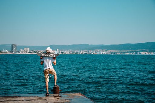 A back view of a man standing on a walkway holding a skateboard