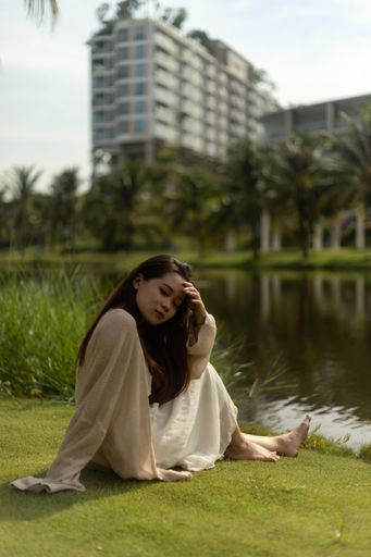 A shallow focus shot of a tired young Asian woman sitting in the grass at the park