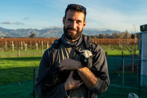 A close-up shot of a man holding a black and white goat in his arms