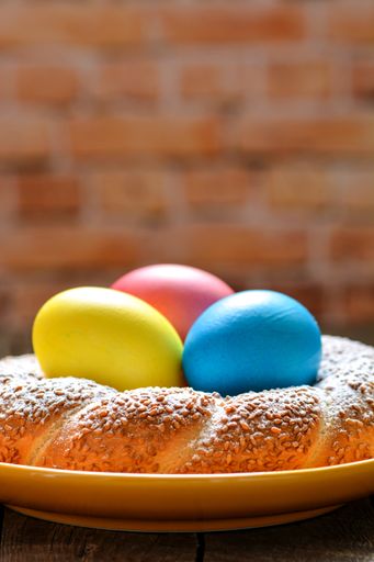 A vertical shot of dyed Easter eggs arranged in the center of freshly baked bun in the blurred background