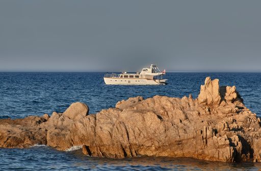 Luxury boat sails off a cliff in the south of Sardinia in a blue sea at sunset.
