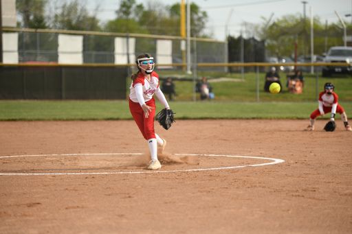 A girl in a red and white uniform catching the ball during the softball match