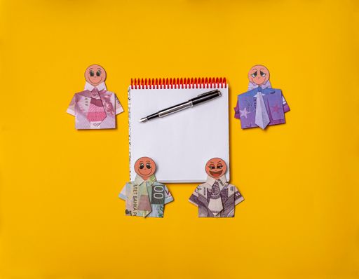 Blank notepad and fountain pen. Around him lie mannequins of happy people in shirts made from paper banknotes from different countries.