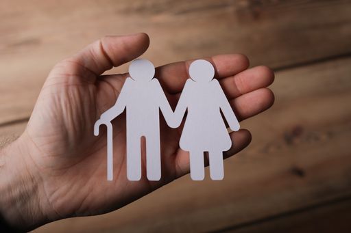 The paper cut of sn old couple in the hands of a man with a wooden background