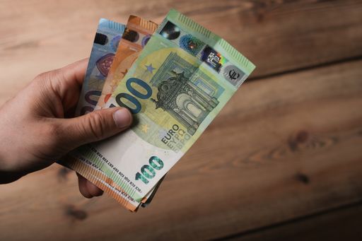 The hands of a man holding European Euro bills with a wooden table on the background
